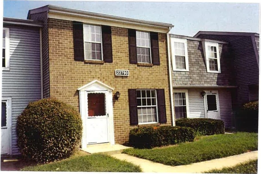 A two-story brick Leonard's Freehold townhouse with a white portico entry and green shrubs