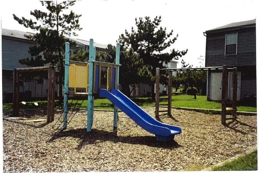 The on-site playground at Leonard's Freehold, with a blue slide and climbing frame among the trees