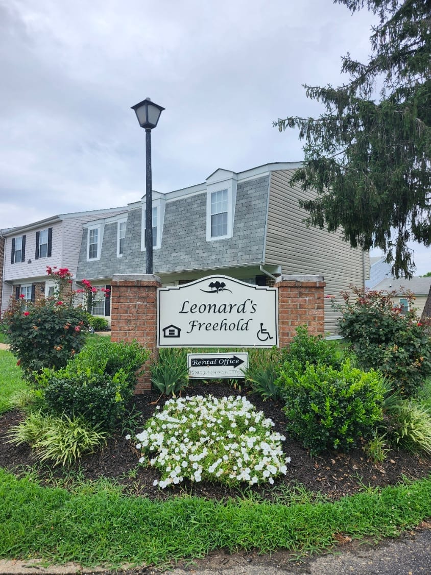 The Leonard's Freehold monument sign on brick pillars, set in a flowering garden bed with a townhouse building behind